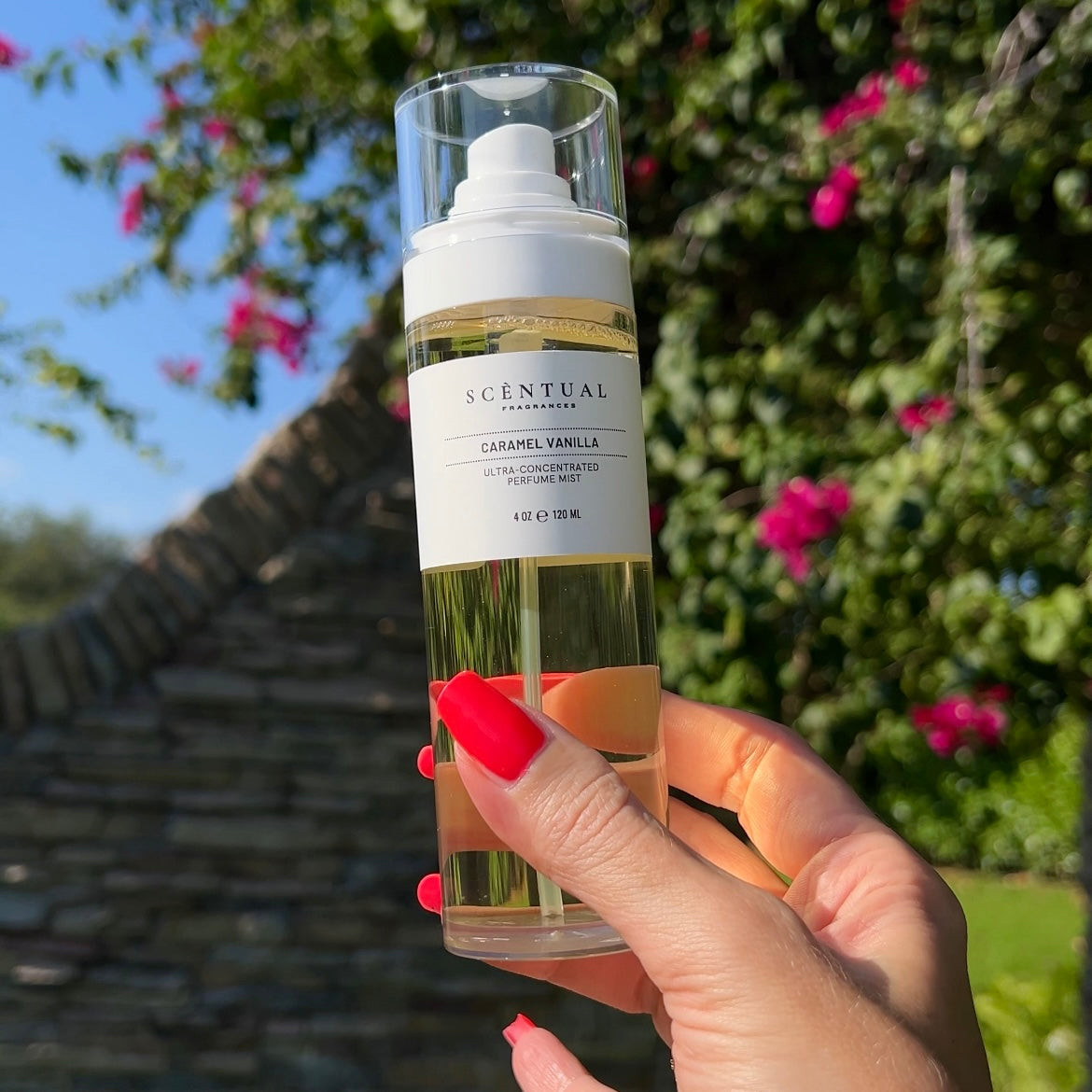 Hand holding a bottle of Scentual Caramel Vanilla perfume with a garden background
